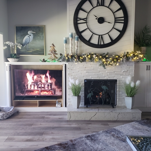 fireplace mantle with large clock face above and screen with fire on side